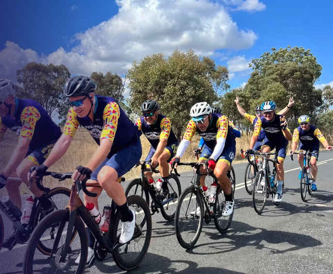 7 cyclists in matching jerseys smiling and laughing as the cycle pass the photographer. The Cyclists are cycling to raise funds for the Mental Wheels Foundation.