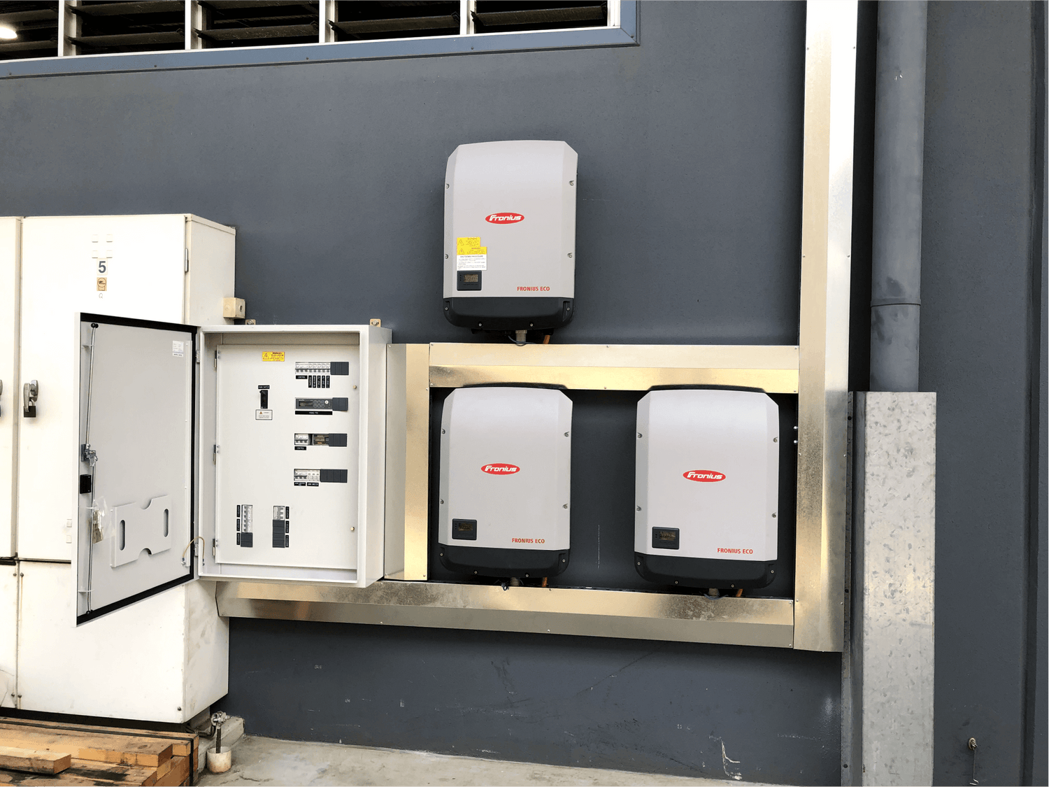 Three Fronius inverters installed on a wall and connected to the meter box of a commercial warehouse, assisting the powering of the factory with solar power.
