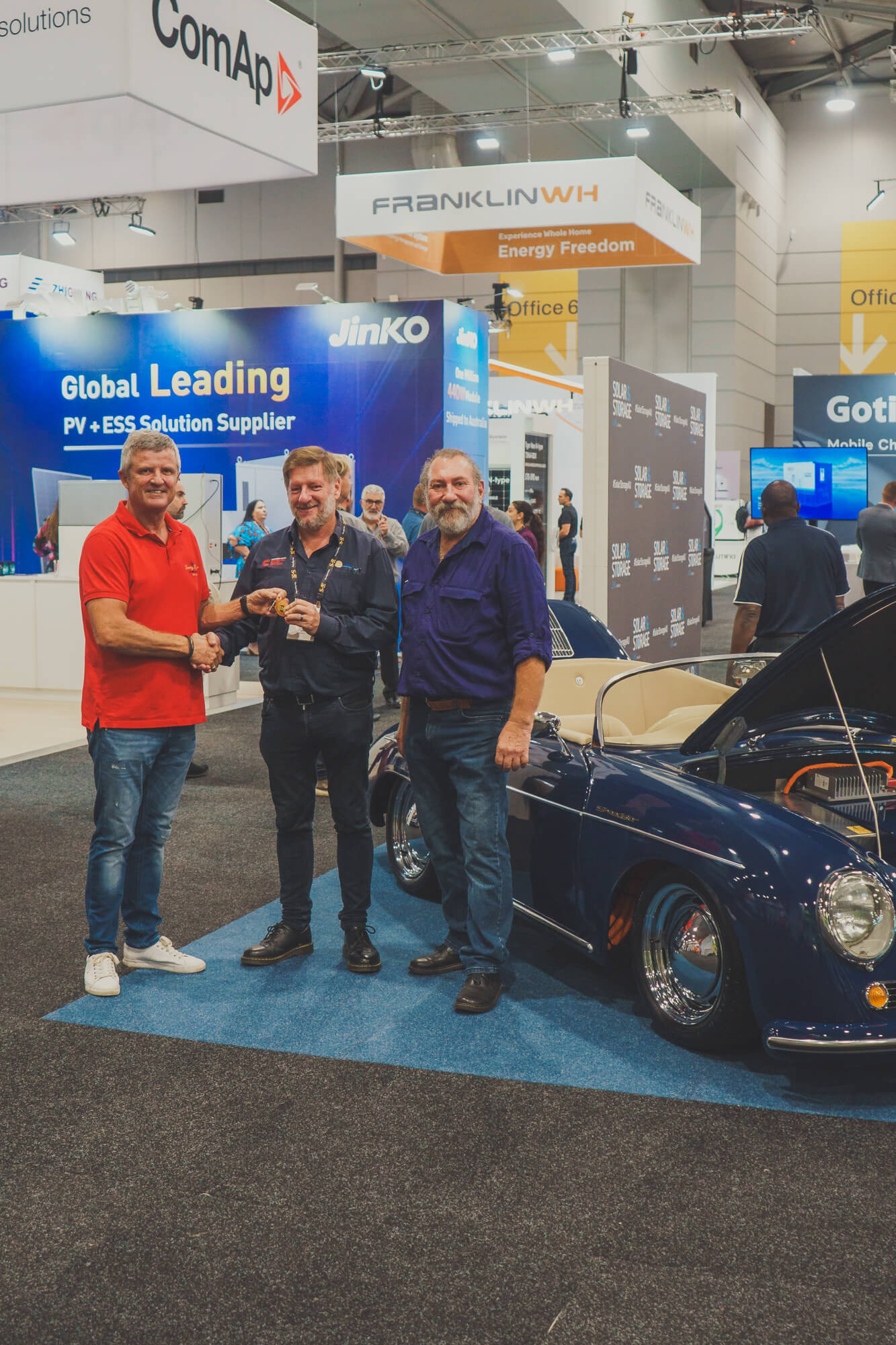 Ian, the Director of UV Power, with Hugo and Chris from REC Kit Cars, discussing all things solar as they laugh and joke behind a blue tribute porsche 365 that has been converted into a solar powered vehicle. The vehicle and men are at the Solar Live and Storage Trade Show.