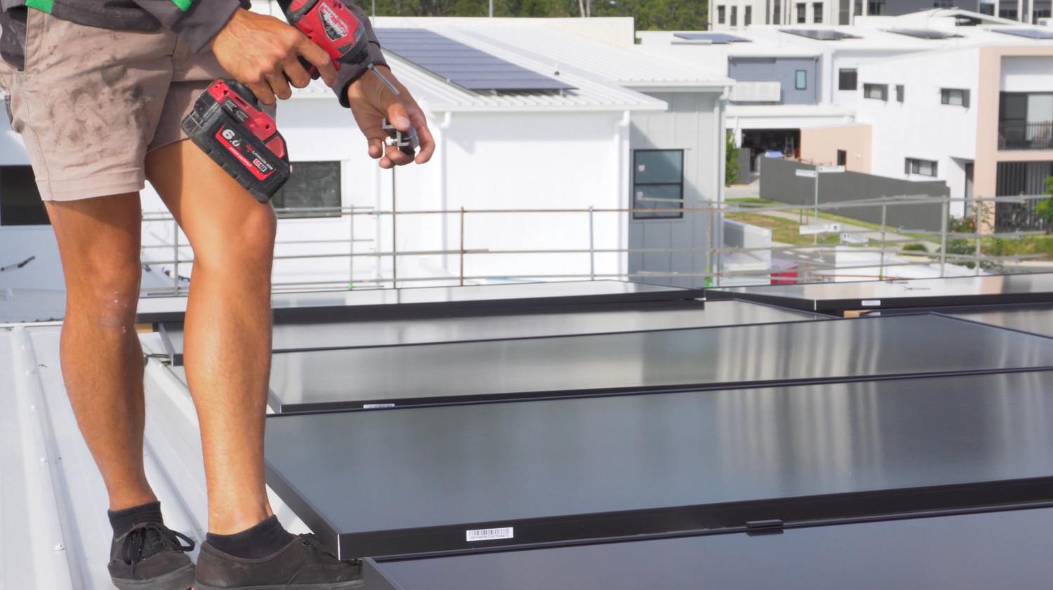 A solar installer on a roof holding a drill tool installing solar panels in Carseldine Village.