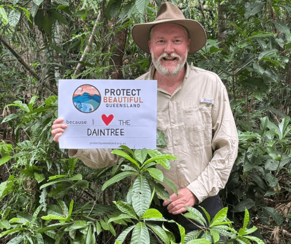A supporter in the rainforest holding a sign reading Protect Beautiful Queensland, because I love the Daintree
