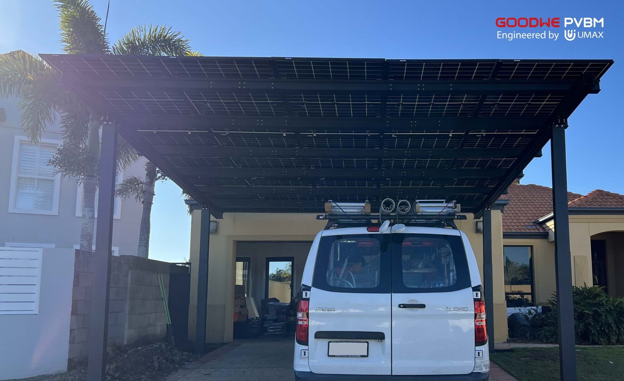 Looking up at a GoodWe Vela double solar carport over a Gold Coast driveway, with a white van parked under the dark frame and panel roof