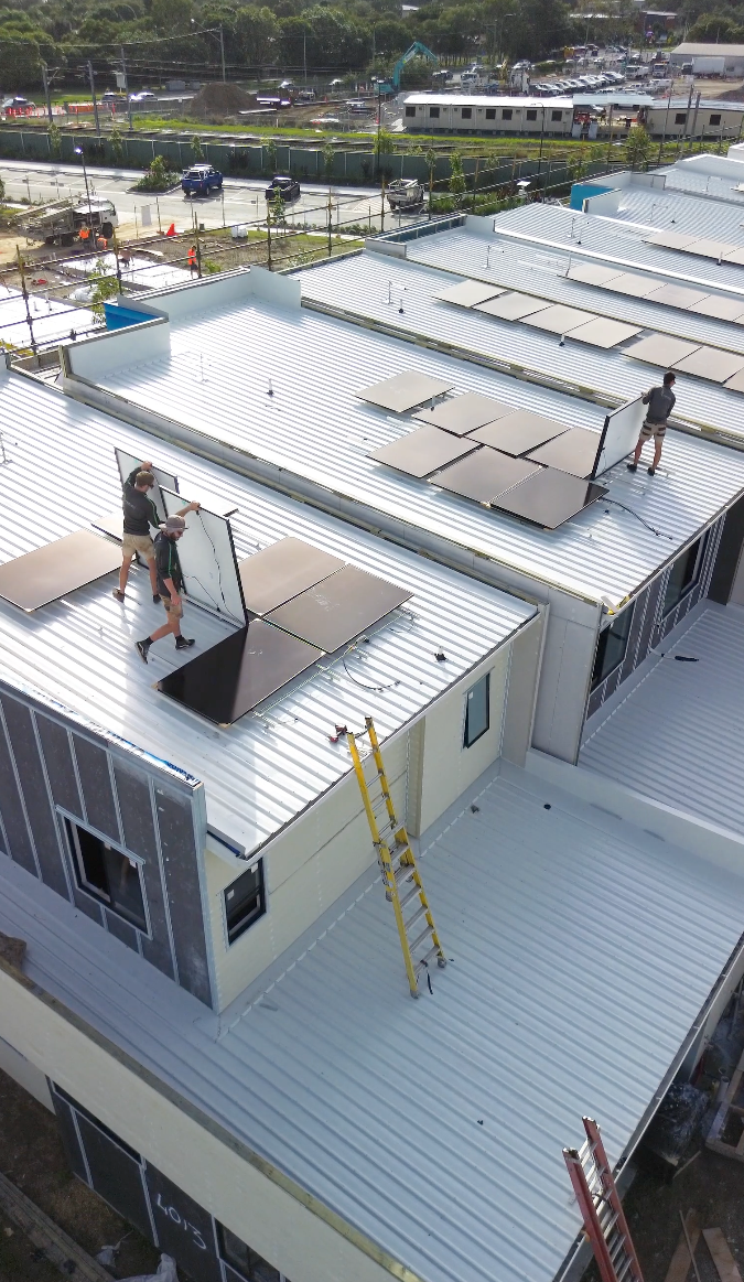 Three solar electricians installing solar panel systems on the rooftops of townhouses in the Carseldine Village residential complex in brisbane.