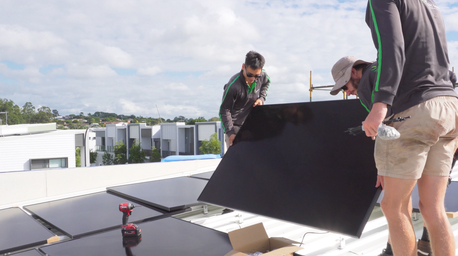 Three solar electricians installing solar panels onto a rooftop in a residential village in Brisbane.