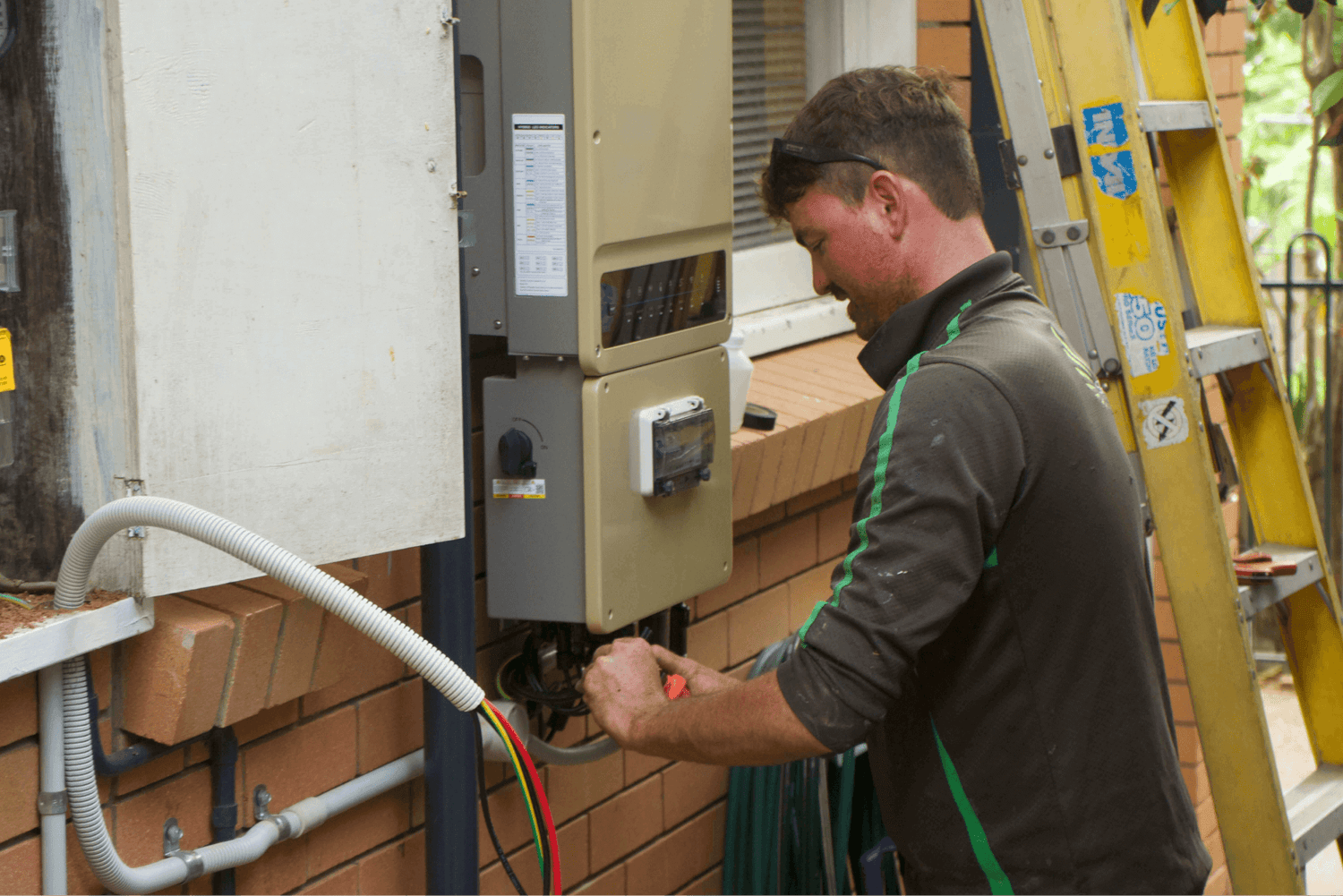 A solar electrician installing a solar battery to a solar inverter, upgrading a solar system in Brisbane.